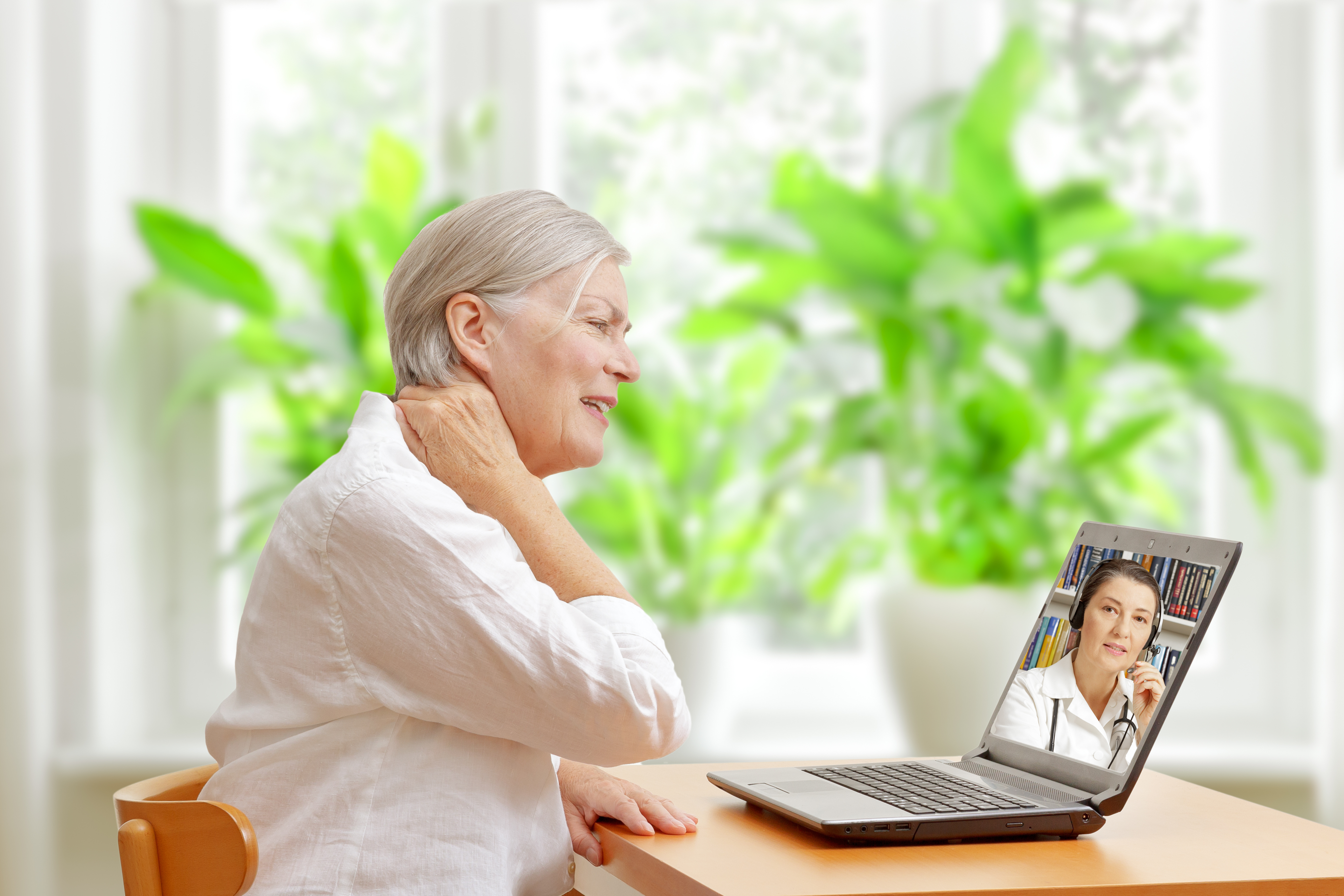 Senior woman in her living room in front of a laptop making a video call with a specialist in orthopedics